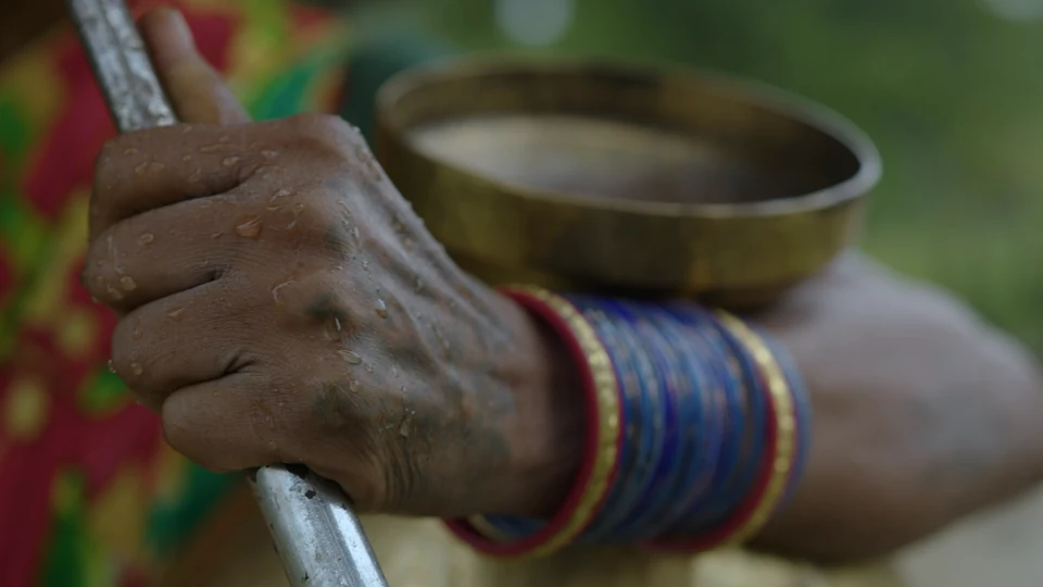 A rain-wet hand holding an umbrella, with bangles and a metal vessel alongside